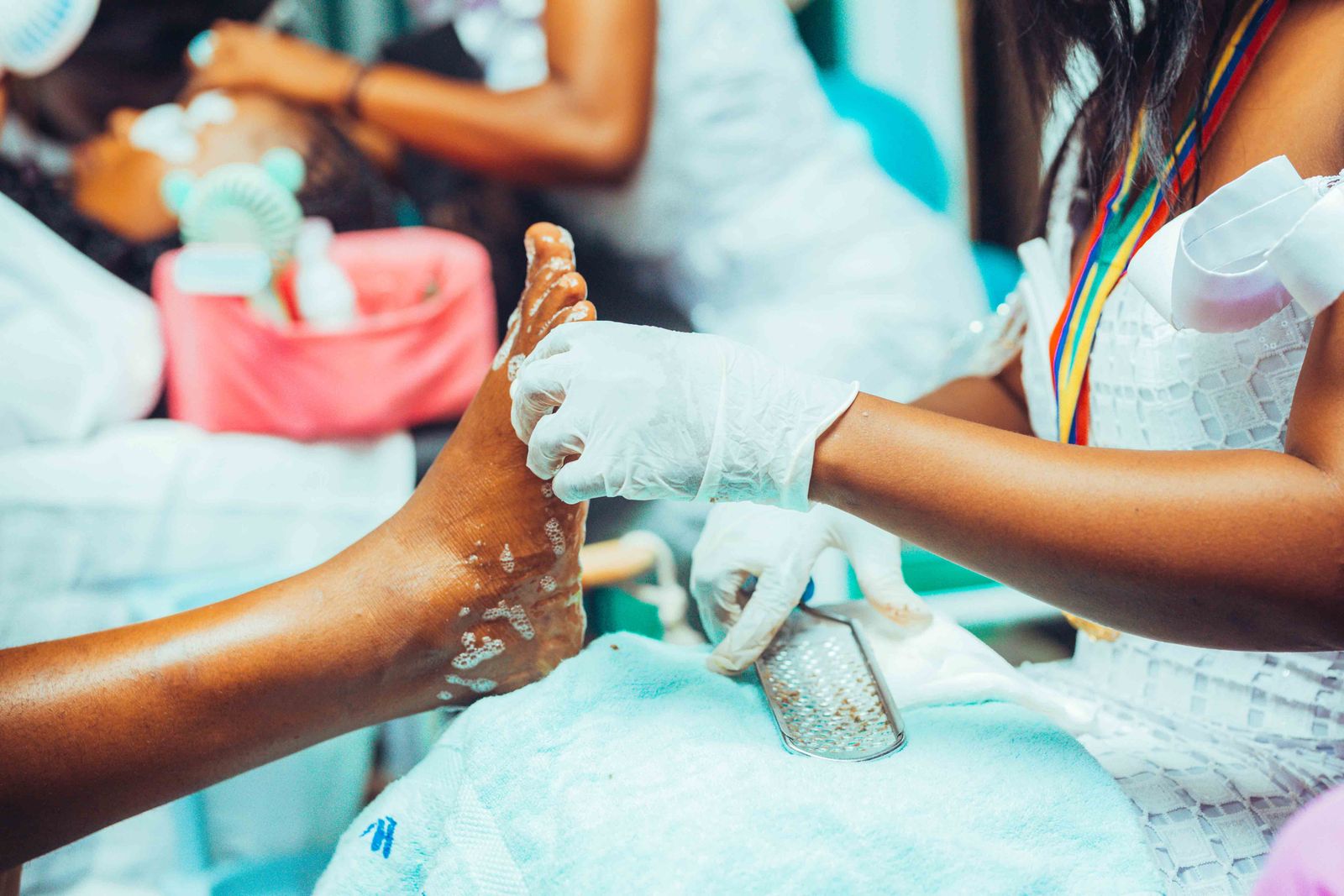 The feet of a client with deep brown skin in an ivory footbath while a technician massages her ankle