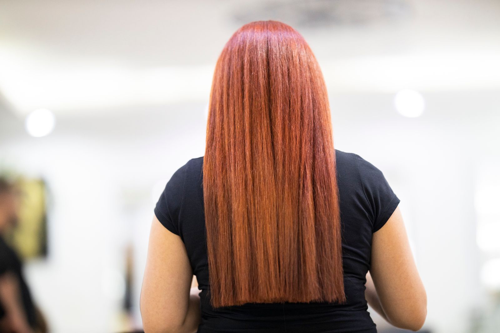 A stylist flat-ironing a glossy silk press through the natural hair of a Black client