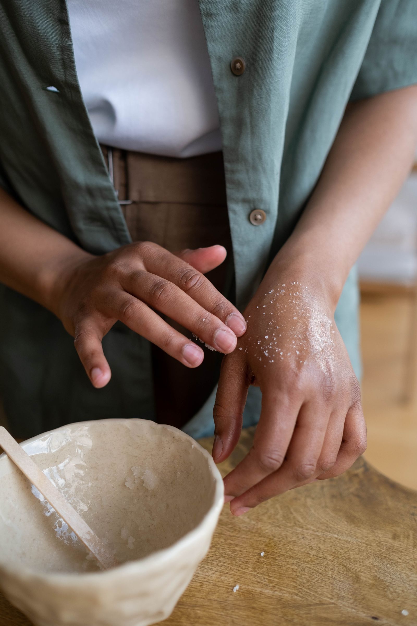 A therapist working a shea and sugar scrub across the shoulder of a woman with deep brown skin beside a brass bowl