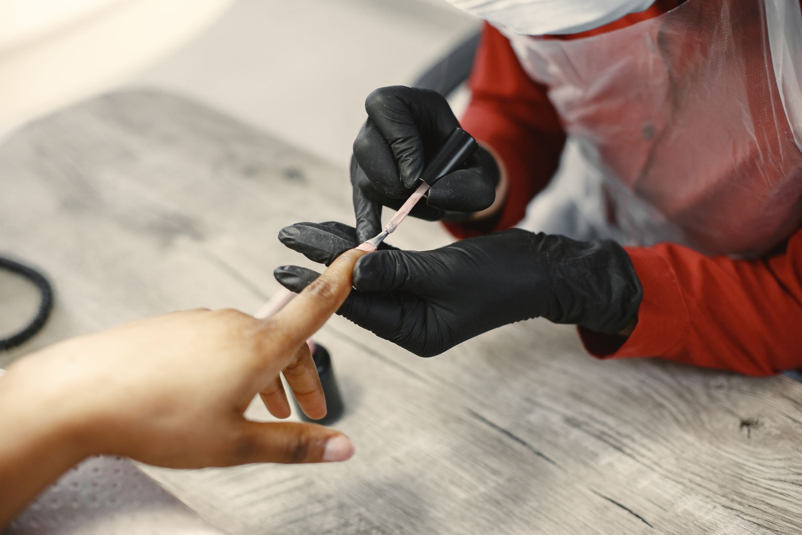 A technician sculpting long almond nail extensions on the hand of a client with deep brown skin
