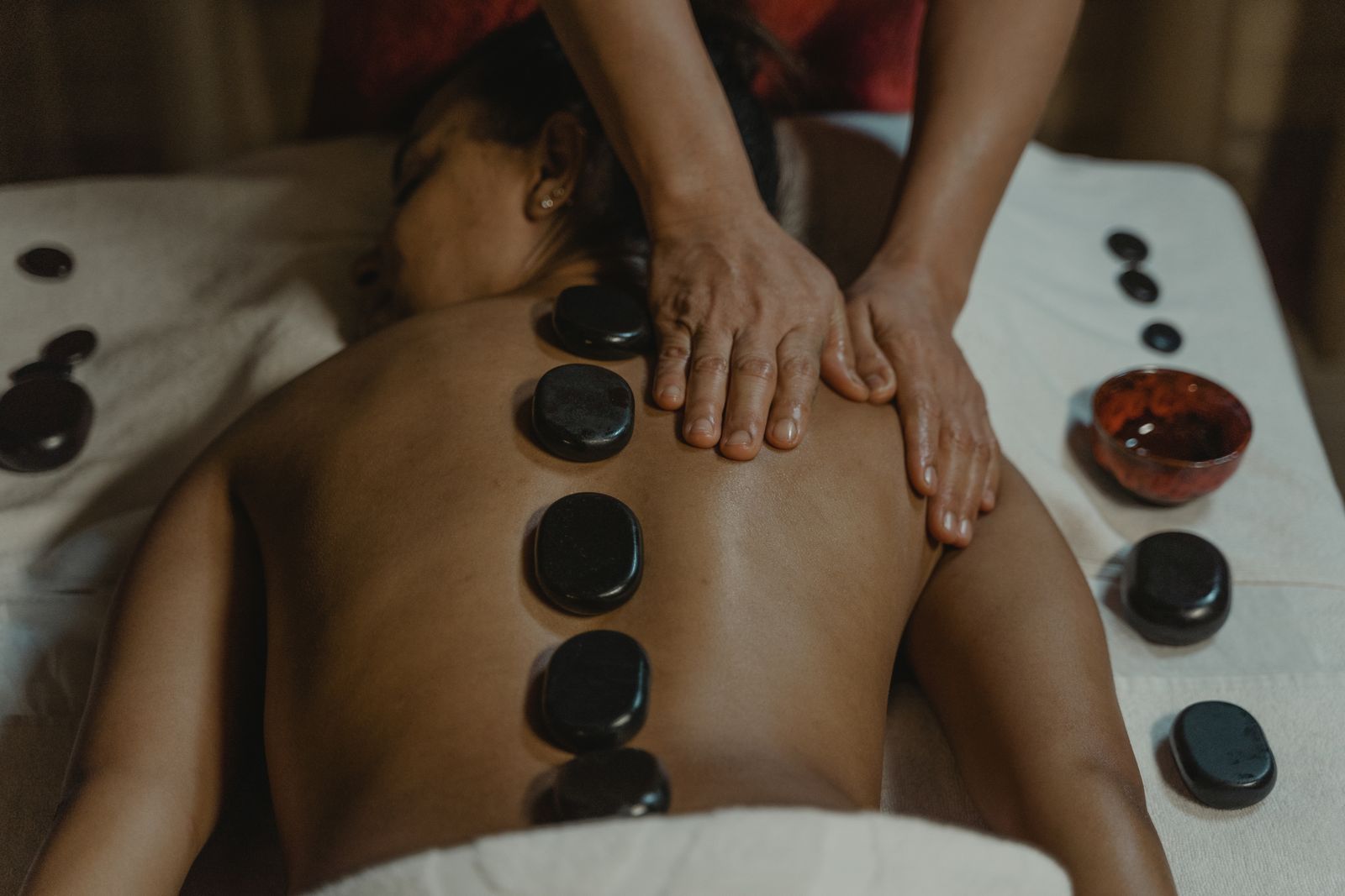 Warm basalt stones laid along the back of a Black client while a therapist places another stone