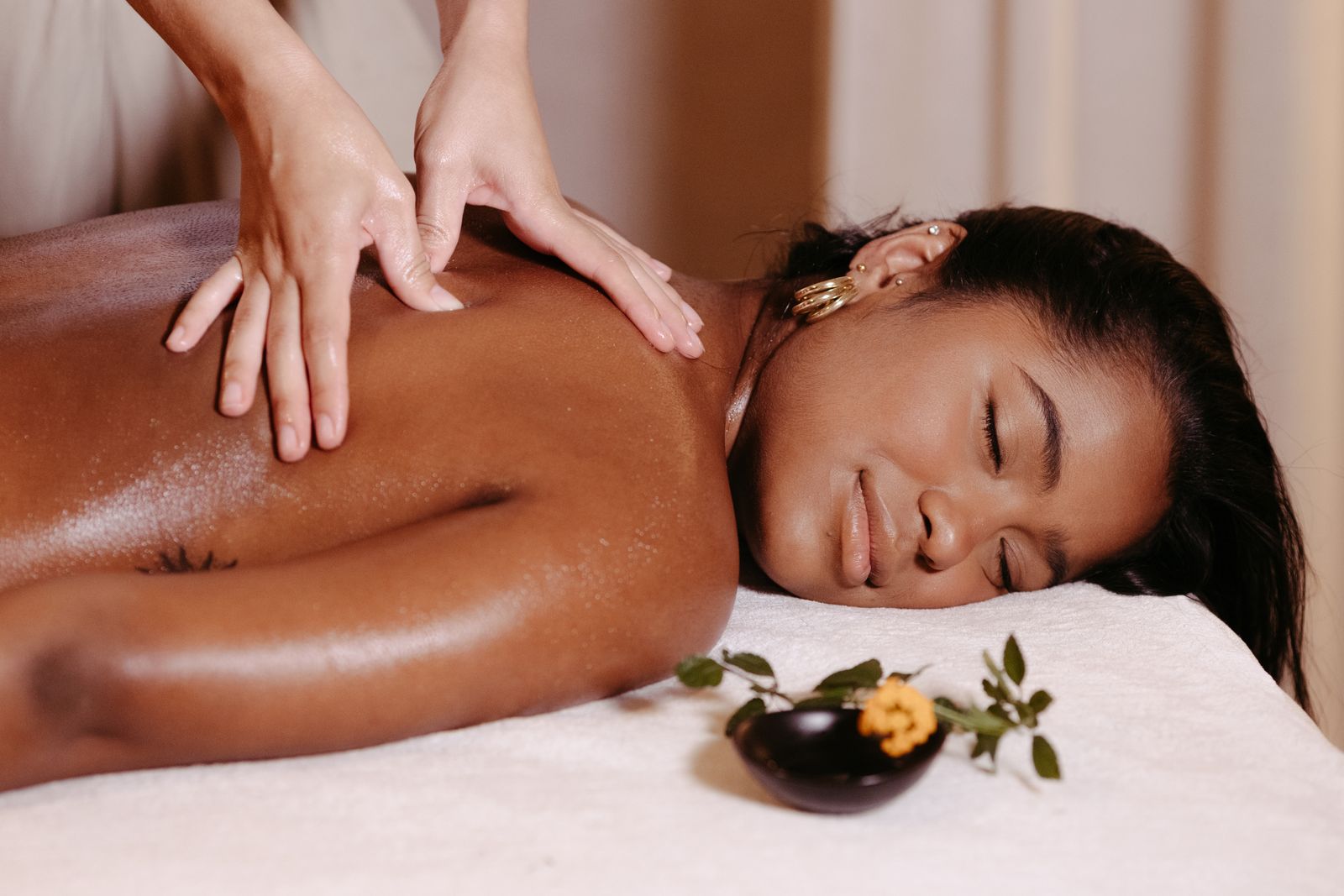 A therapist performing long Swedish massage strokes across the oiled back of a Black woman on a candlelit treatment bed