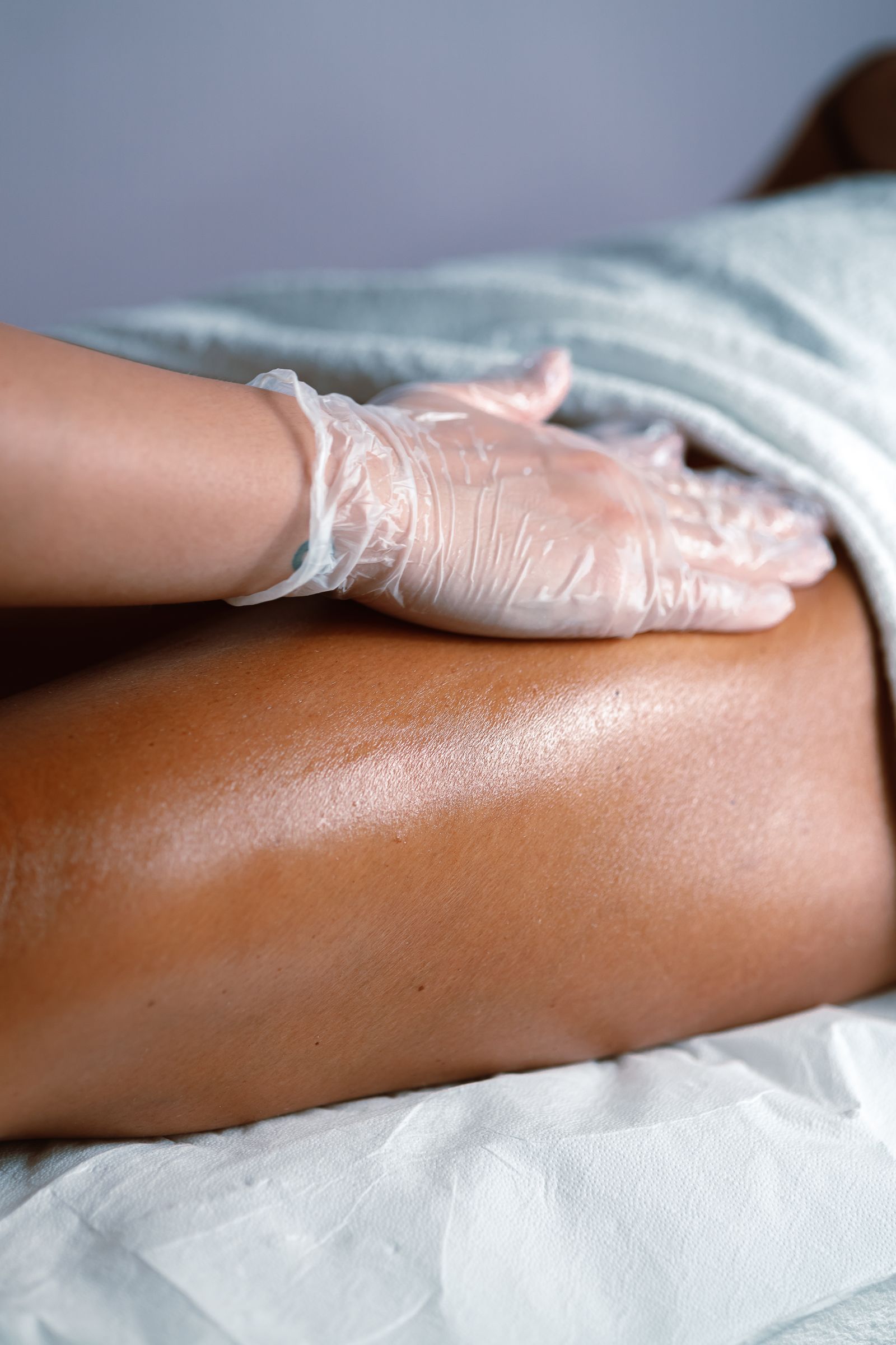 A gloved therapist smoothing warm wax along the lower leg of a client with deep brown skin